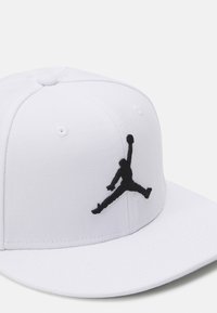 Hvid hat lavet af stof med struktureret design. Har et sort broderet Jumpman-logo. Inkluderer lufthuller på kronen.
