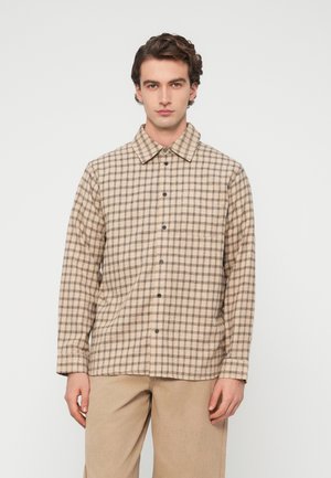 Καρό μπεζ πουκάμισο φανέλας με κουμπιά μπροστά, γιακά και μακριά μανίκια. Υποτονικές καφέ αποχρώσεις στο σχέδιο. Ομαλή υφή.