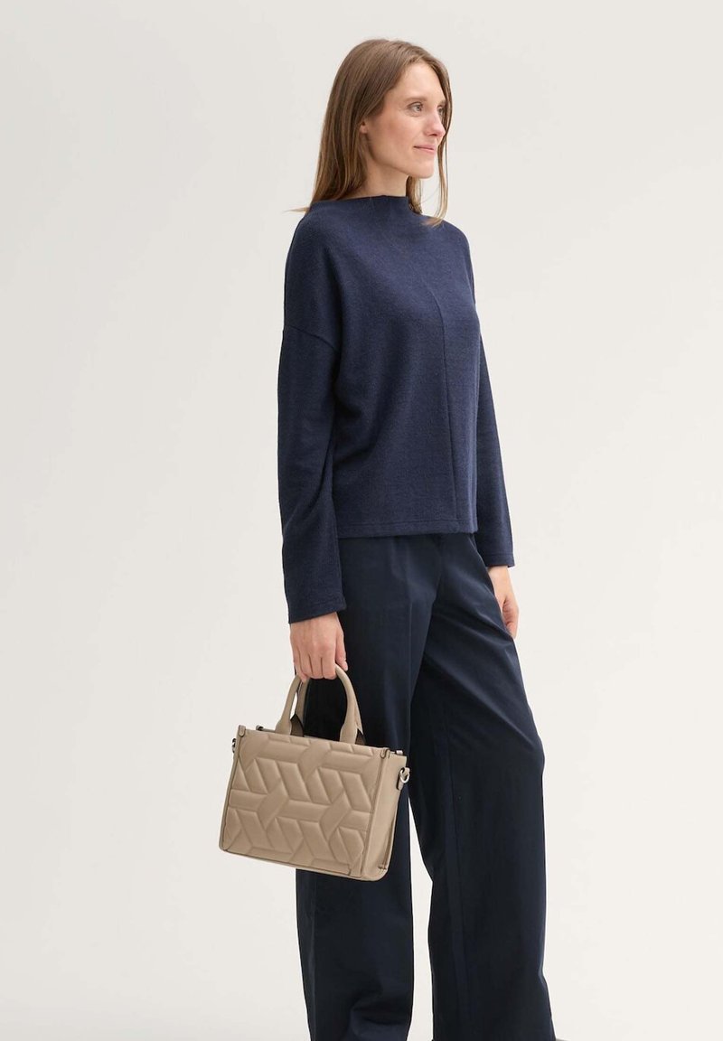 Pull en maille côtelée marine avec un col montant, associé à un pantalon large noir et un sac à main en toile beige clair à motif géométrique.