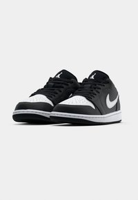 Black and white sneakers with a smooth leather upper, perforated toe box, black laces, and a silver Nike swoosh. Features a rubber sole.