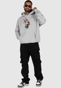 Szary hoodie z grafiką przedstawiającą rzeźbę trzymającą wagę i miecz; w zestawieniu z czarnymi spodniami cargo oraz czarno-białymi sneakersami.