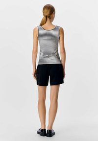 Top de tirantes a rayas en blanco y negro, combinado con pantalones cortos negros. La tela parece ligera y ajustada, con un escote redondeado y un diseño minimalista.