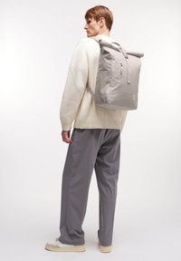 Grå rulltoppsryggsäck i slitstarkt tyg, med justerbara remmar, en framficka och en slät, minimalistisk design.