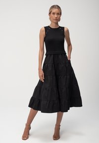 Czarna sukienka z prążkowanym, bezrękawnikowym topem z guzikami oraz warstwową, zwiewną spódnicą wykonaną z gładkiego materiału.