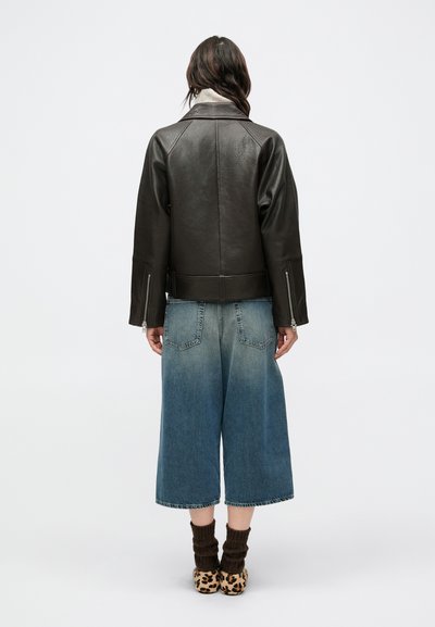 Bruine leren jas met een kraag, wijde mouwen en ritsdetails, gecombineerd met wijde blauwe denim culottes en schoenen met dierenprint.