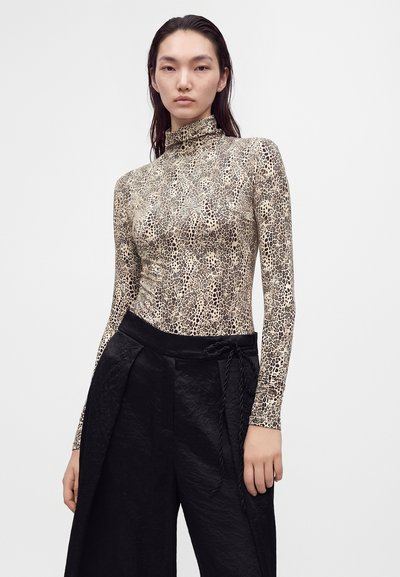 Femme aux longs cheveux foncés portant un haut à col montant, manches longues imprimé léopard et un pantalon noir ample avec une ceinture nouée.