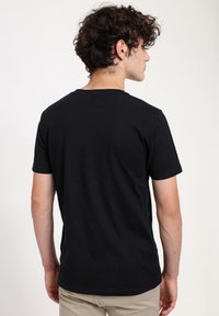 Černé bavlněné tričko s kulatým výstřihem, krátkými rukávy a volným střihem. Viditelné švy a hladká textura.