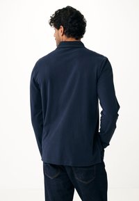 Polo a maniche lunghe blu navy con una texture morbida e colletto. Presenta un orlo dritto ed è abbinato a pantaloni in denim scuro.
