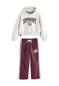Felpa cropped grigia con la scritta "SUPERDRY OSAKA" in testo bordeaux, abbinata a pantaloni della tuta marroni con strisce laterali e cordino bianco.