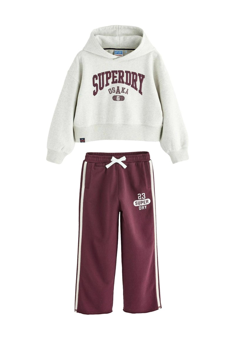Felpa cropped grigia con la scritta "SUPERDRY OSAKA" in testo bordeaux, abbinata a pantaloni della tuta marroni con strisce laterali e cordino bianco.
