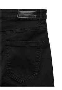 Vue arrière d’un jean en denim noir avec une poche arrière cousue et une étiquette de marque en cuir noir portant l’inscription « VERO MODA DENIM ».