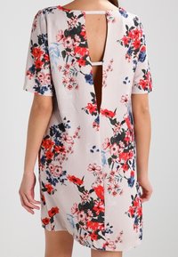 Květinové šaty z jemného materiálu mají krátké rukávy, hluboké výstřih vzadu a vícebarevné květinové vzory v odstínech červené, růžové a modré.