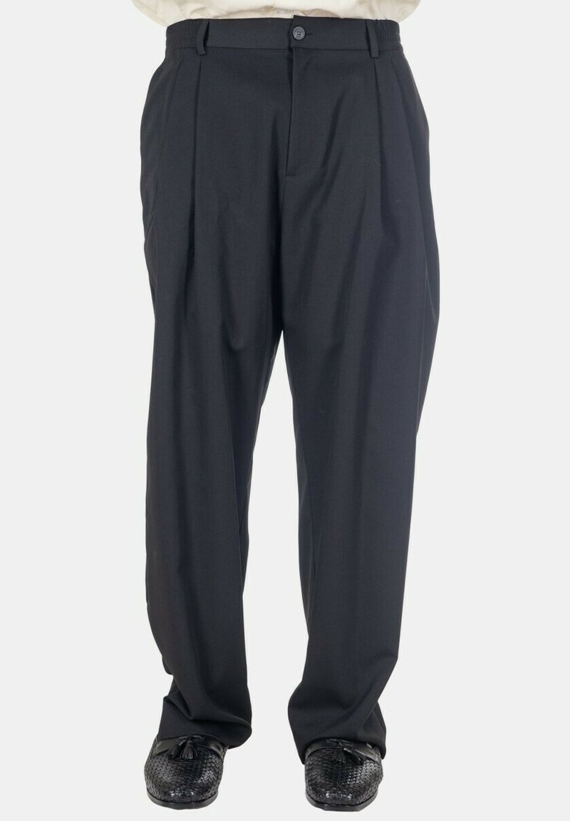 Pantalon noir plissé avec fermeture à bouton et fermeture éclair, porté avec des mocassins noirs à pampilles texturées.