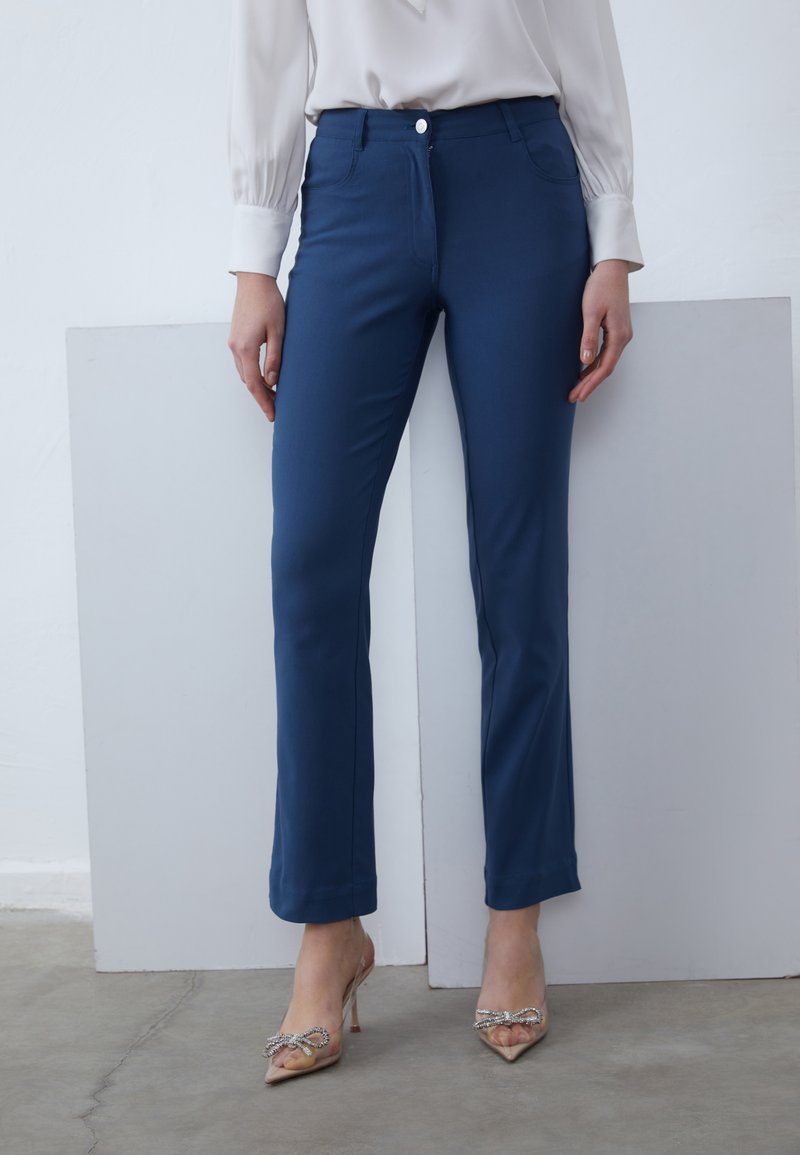 Pantalon ajusté bleu marine en tissu extensible, doté d'une fermeture éclair à l'avant, d'un bouton et de poches latérales.
