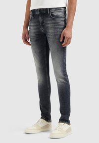 Slim-fit jeans van donkergrijze denim met een vervaagde afwerking. Heeft een vijf-pocket ontwerp en metalen hardware. Gedragen met witte sneakers.