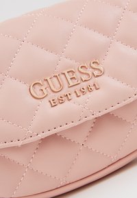 Różowa pikowana torebka z eko-skóry, z złotym logo i detalami przeszyć. Projekt obejmuje klapę zamykającą.