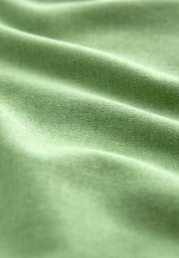 Textil de color verde claro con una textura suave y lisa, que presenta pliegues suaves y un patrón de punto consistente en todo el material.
