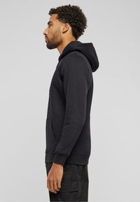 Zwarte hooded sweatshirt met een kangoeroezak, ribgebreide manchetten en een gladde textuur, zijaanzicht tegen een neutrale achtergrond.