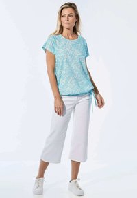 Lichtblauw gepatternde shirt met korte mouwen, ronde halslijn en strikdetail, gecombineerd met witte wijde broek en witte sneakers.