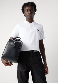 Schwarzer Leder-Rucksack mit runder Form und Oberhandgriff, kombiniert mit einem weißen Poloshirt und dunklen Jeans, mit einem dezenten Logo.