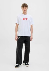 Baltas medvilnės marškinėlis su raudonu "UFC" logotipu, derinamas su juodomis plačiomis kelnėmis, turinčiomis sidabrinį grandinėlės detalę. Išvaizdą baigia juodai balti sportbačiai.