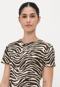 T-shirt a maniche corte a strisce zebra marroni e crema con colletto rotondo. Il tessuto appare morbido e leggero, con una texture liscia.