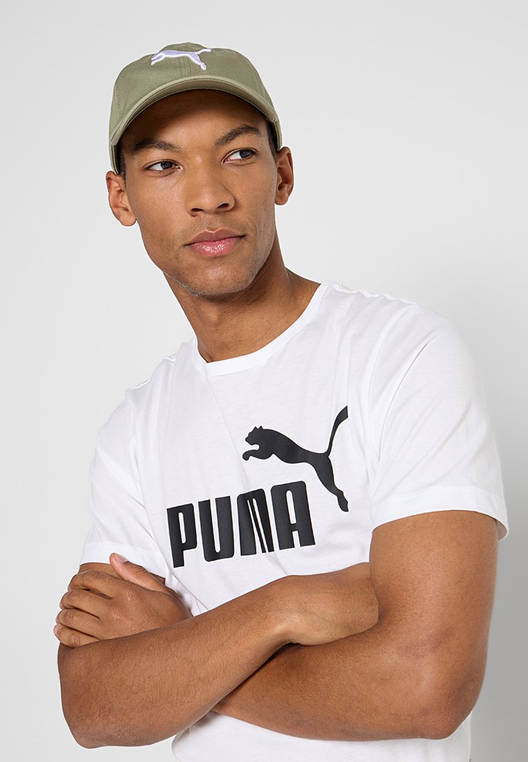 Gorra de béisbol color caqui con logo bordado en blanco, combinada con una camiseta blanca de manga corta que presenta un gran logo negro en el frente.