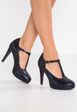 Sorte højhælede sko med T-strop design, blank lædertekstur, spændefunktion og rund tå.