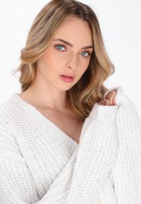 Pulover alb tricotat cu un model texturat și decolteu larg în formă de V. Are mâneci supradimensionate și un detaliu subtil cu nasturi.