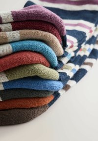Stapel von sieben gestrickten Socken in verschiedenen Farben: burgunderrot, beige, blau, grün, rot, orange und braun; mit gestreiften Mustern und gerippten Kanten.