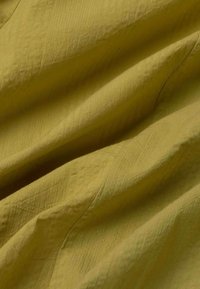 Tissu vert olive froissé avec coutures visibles et texture douce, présenté en gros plan.
