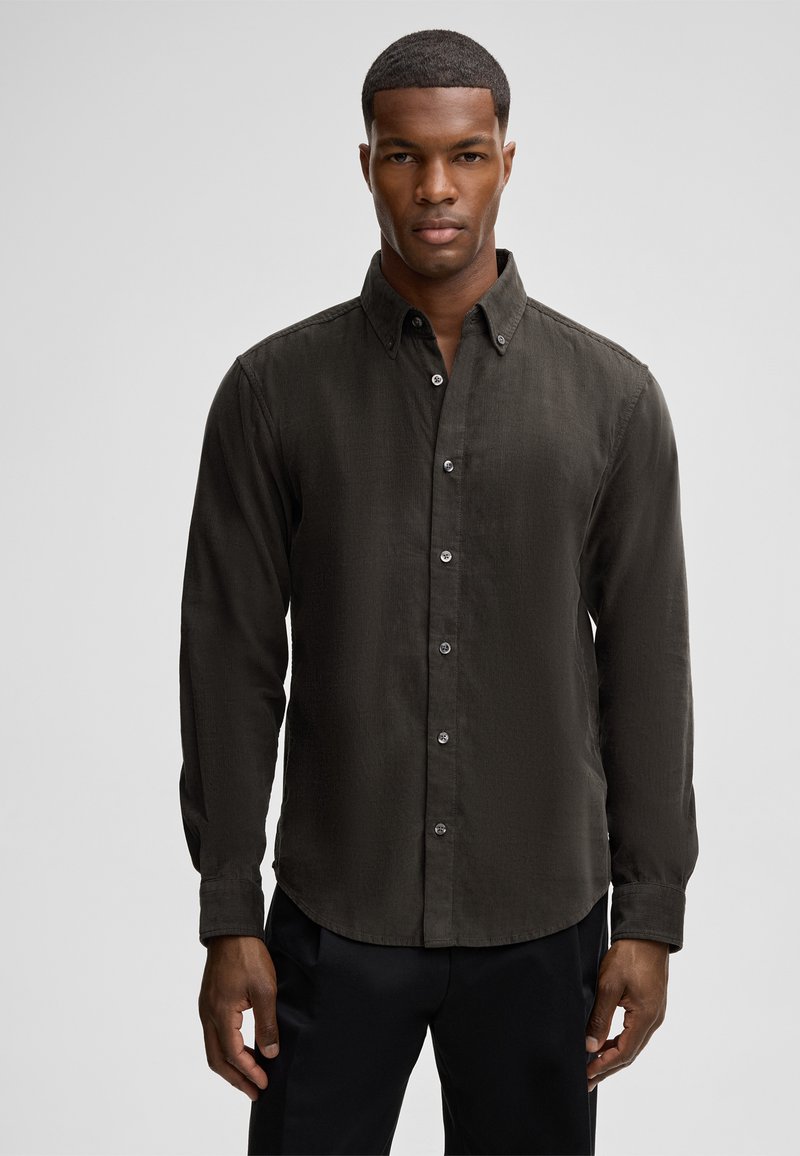 Camicia button-up verde scuro con tessuto testurizzato, maniche lunghe e colletto a punta. Presenta bottoni argentati lungo la parte anteriore.