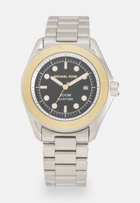 Reloj de acero inoxidable plateado con esfera negra, bisel dorado y cara redonda. Presenta marcadores de horas, ventana de fecha y una pulsera de eslabones metálicos.