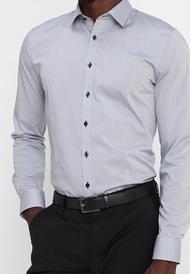 Vaaleanharmaa napitettava paita, jossa on jämäkkä kaulus, mustat napit ja hienovarainen tekstuuri, yhdistettynä mustiin housuihin ja vyöhön.