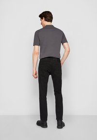 Juodi džinsai ir trumpomis rankovėmis pilkas polo marškinėliai. Džinsai turi klasikės kirpimą, su dviem užpakalinėmis kišenėmis. Modelis vilki juodus aulinukus.