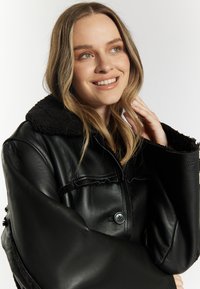 Sort læderjakke med en struktureret sort shearlingkrave, knaplukning og cropped ærmer med flæsekanter. Glat finish overalt.