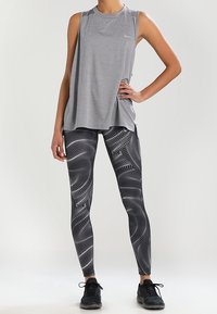 Top de entrenamiento gris combinado con leggings negros con un patrón ondulado en blanco. Incluye zapatillas negras y un diseño de corte relajado.
