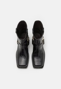 Botines negros de tobillo hechos de cuero brillante con estampado de cocodrilo. Punta cuadrada, tacón bajo y detalles en tono dorado.