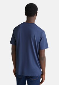 Námořnická modrá krátkosrstá tričko vyrobené z bavlny s kulatým výstřihem, hladkou texturou a uvolněným střihem, zobrazené zezadu.