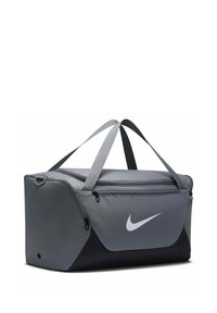 Γκρι και μαύρη τσάντα Nike με φερμουάρ στην κορυφή και πλαϊνές τσέπες, ιμάντες μεταφοράς και λευκό λογότυπο Swoosh στο μπροστινό πάνελ.