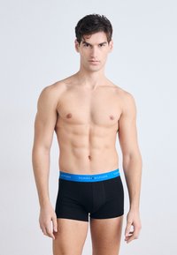 Boxer shorts noirs avec une ceinture bleue portant la marque "TOMMY HILFIGER", présentés sur un modèle avec un fond neutre.