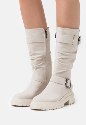 Bottes hautes blanches en simili cuir avec un design décontracté, fermeture éclair sur le côté et accents de boucle. Semelle épaisse avec un motif de crampons texturé.