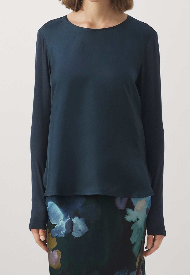 Navy blue pitkähihaine paita, jossa on sileä pinta ja pyöreä kaula-aukko. Alamarginaali on hieman epäsymmetrinen, ja se on yhdistetty kukkakuosiset hameeseen.