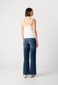 White ribbed tank top with scalloped lace straps, paired with light blue flared denim jeans. Simple design and clean color contrast.