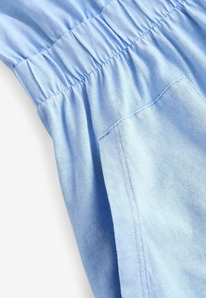 Tissu en coton bleu clair avec taille élastique froncée, présentant une poche latérale et une texture lisse, montré sous un angle pour plus de détails.