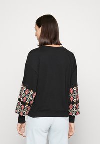 Sweatshirt preto com mangas balão bordadas em padrões geométricos coloridos. Tecido macio com um corte descontraído e punhos canelados.