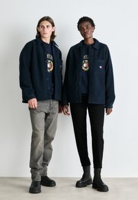 Chaquetas de forro polar navy con cierres de botones, llevadas sobre sudaderas oscuras y combinadas con pantalones grises y negros, con botas negras gruesas.