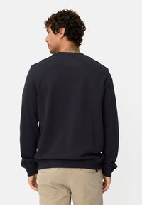 Sweat-shirt bleu marine à manches longues, poignets et ourlet côtelés, et col rond. Présente une texture subtile et des détails cousus sur les épaules.