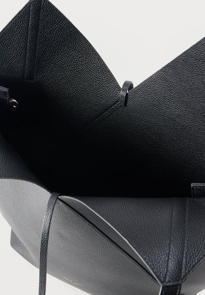 Μαύρη τσάντα ώμου από δέρμα με υφή, με ευρύ ανοιχτό πάνω μέρος και λεπτούς ιμάντες ώμου, σε ανοιχτό φόντο.