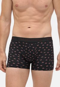 Torso masculino que lleva puesta una braguita negra con un patrón de bicicletas en rojo y blanco y una cinturilla de marca.